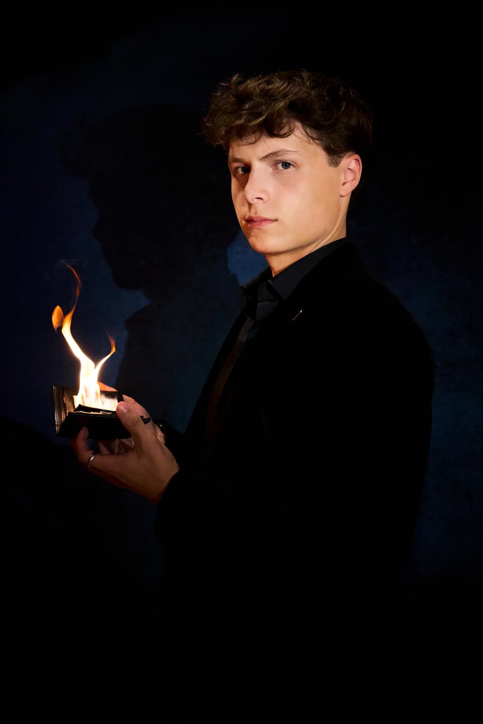 Studio-portret van Sven Manders in donker kostuum met een opengeslagen portemonnee waar vlammen uit slaan
