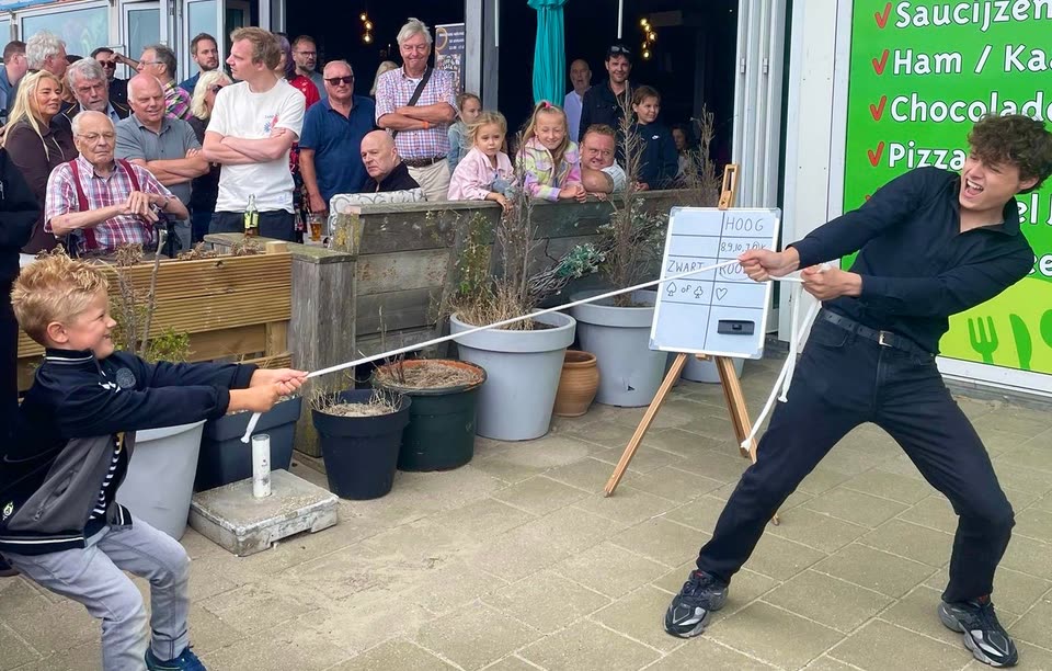 Een jonge vrijwilliger en Sven Manders trekken tijdens een buitenshow allebei aan een touw, omringd door publiek